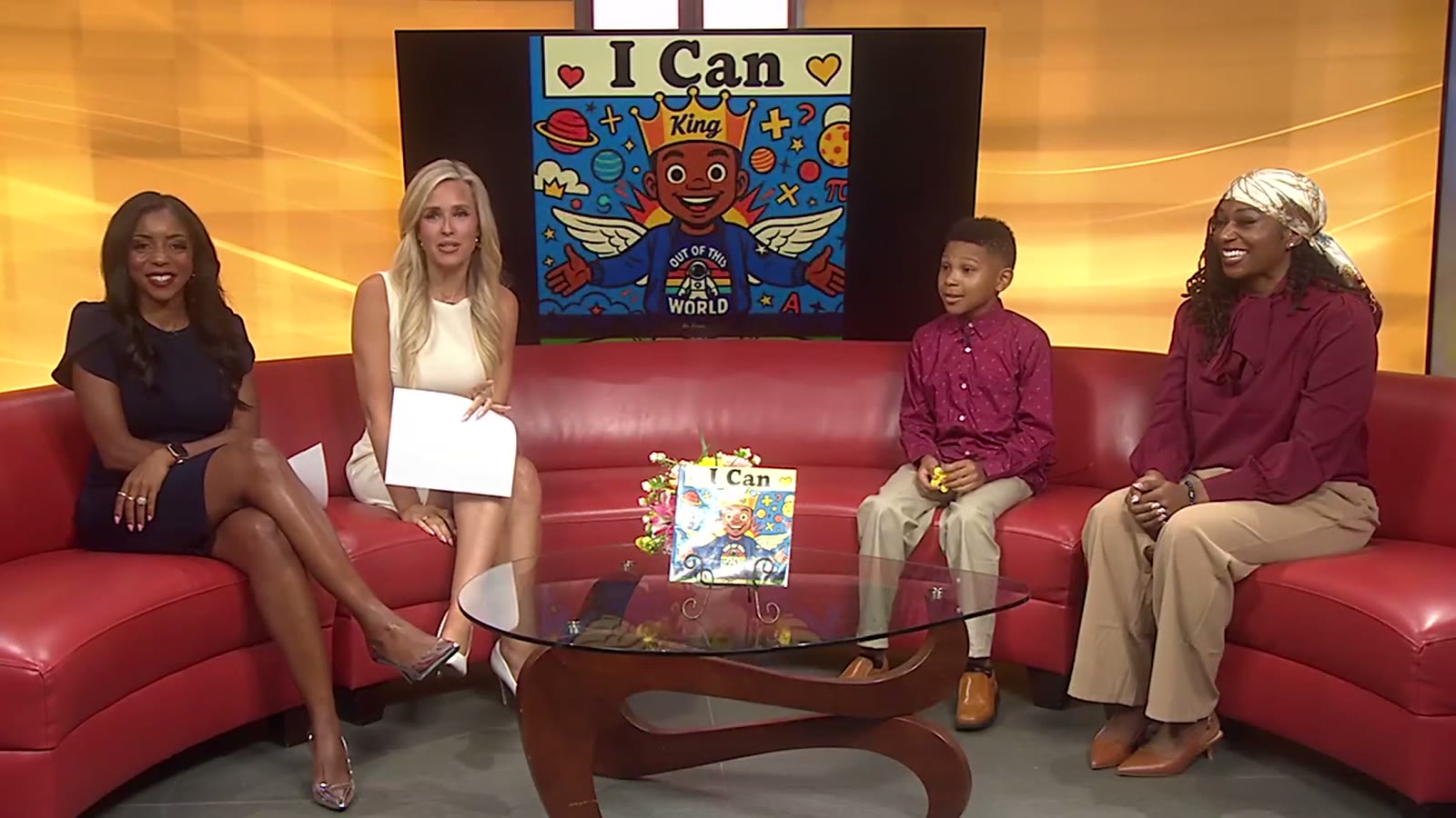 Titan Glover and his mom Lauren Motley on the Good Day Columbus set with the two anchors, the I Can book cover on the studio screen behind them and the book displayed on the table.
